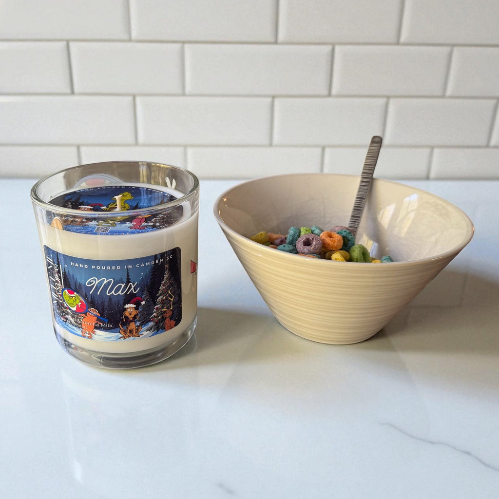 Candle labeled 'Max' next to a bowl of cereal with a spoon on a white surface.