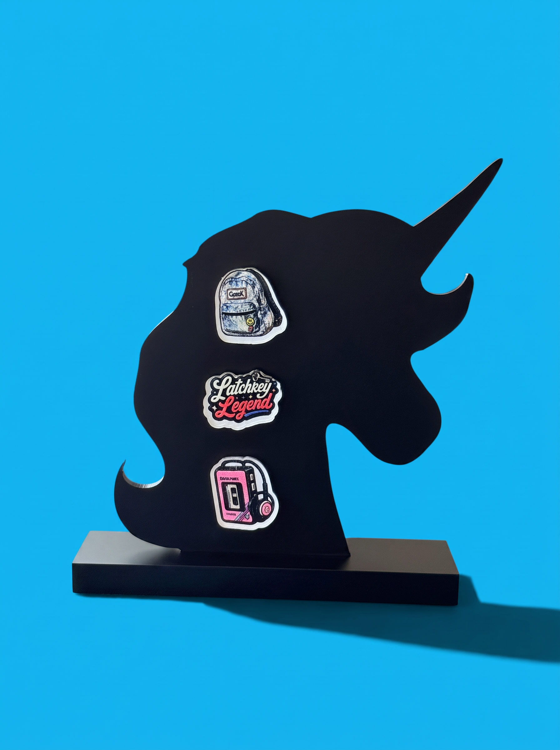 A black unicorn-shaped display stand on a rectangular base, featuring three decorative earrings, photographed against a bright blue background.