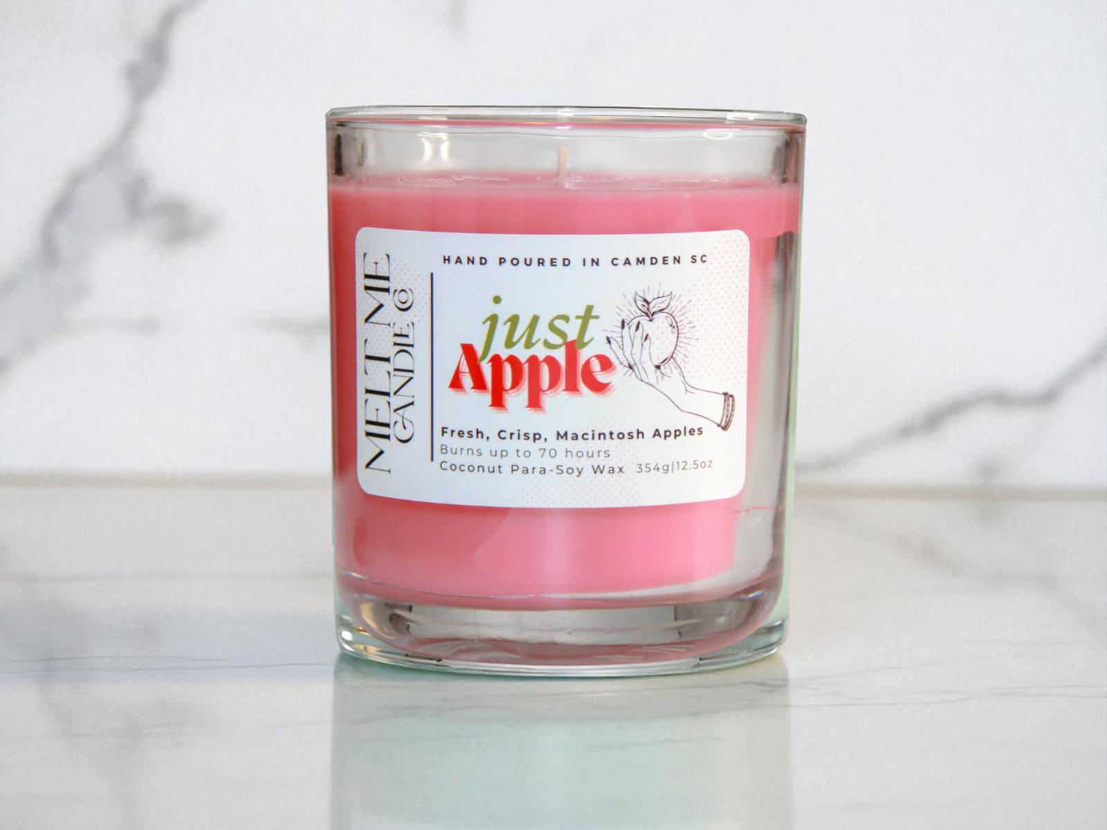 Red candle in a glass jar with a 'Just Apple' label on a white marble surface