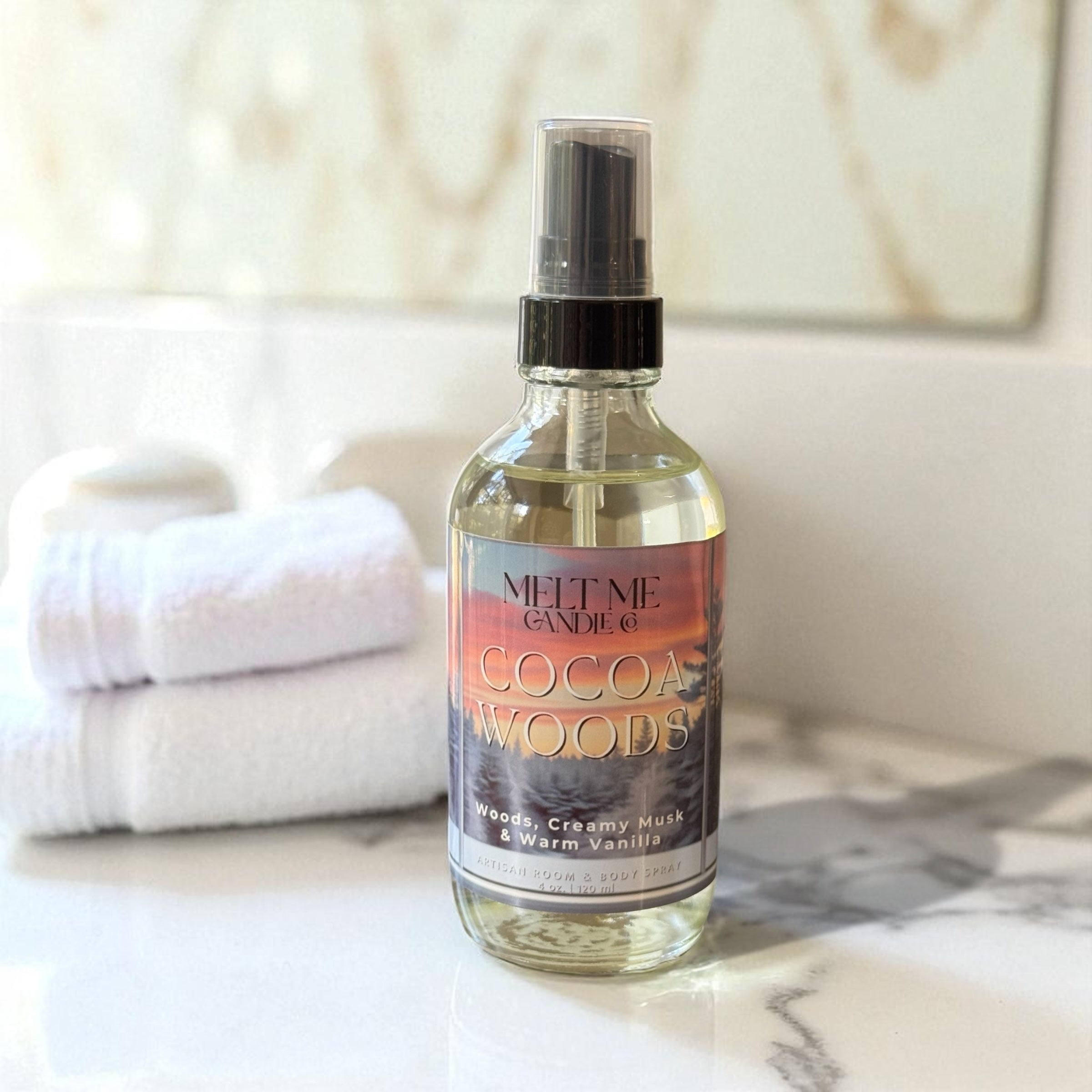 Bottle of 'Cocoa Woods' spray on a marble surface with towels in the background