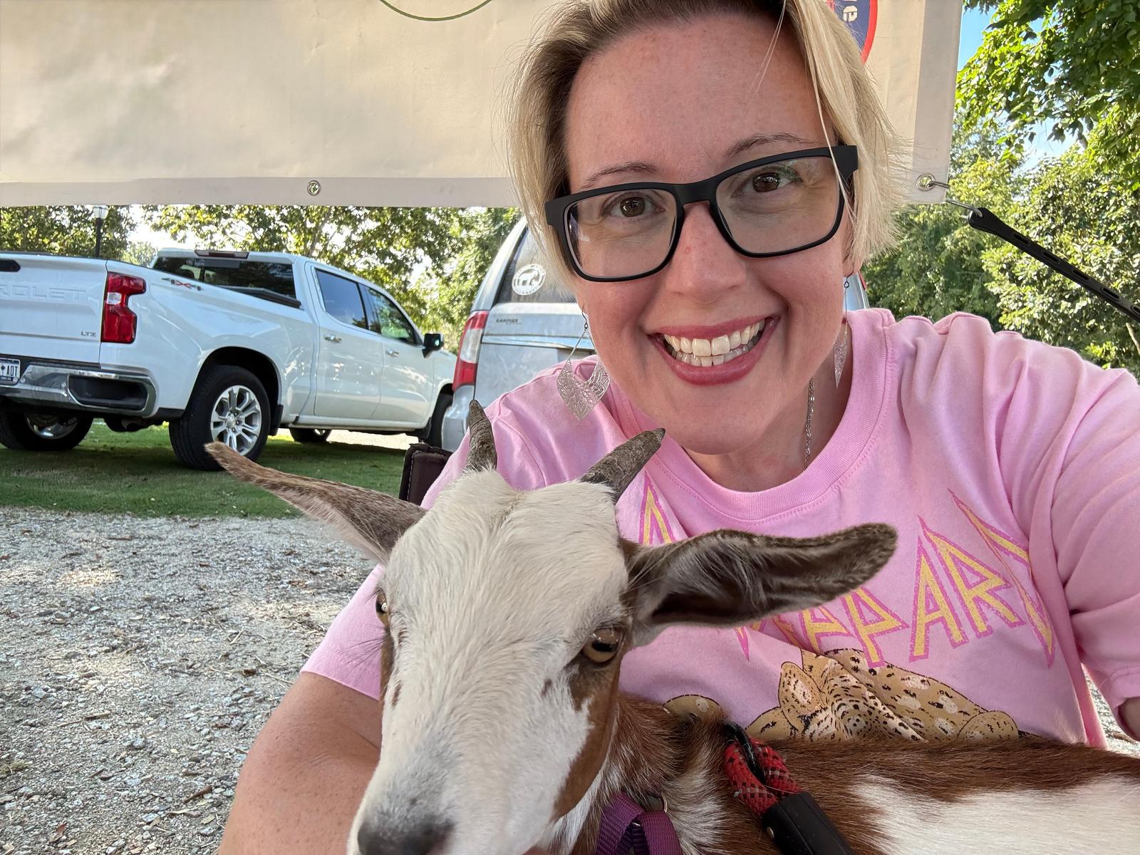 Woman in pink shirt with a goat in an outdoor setting