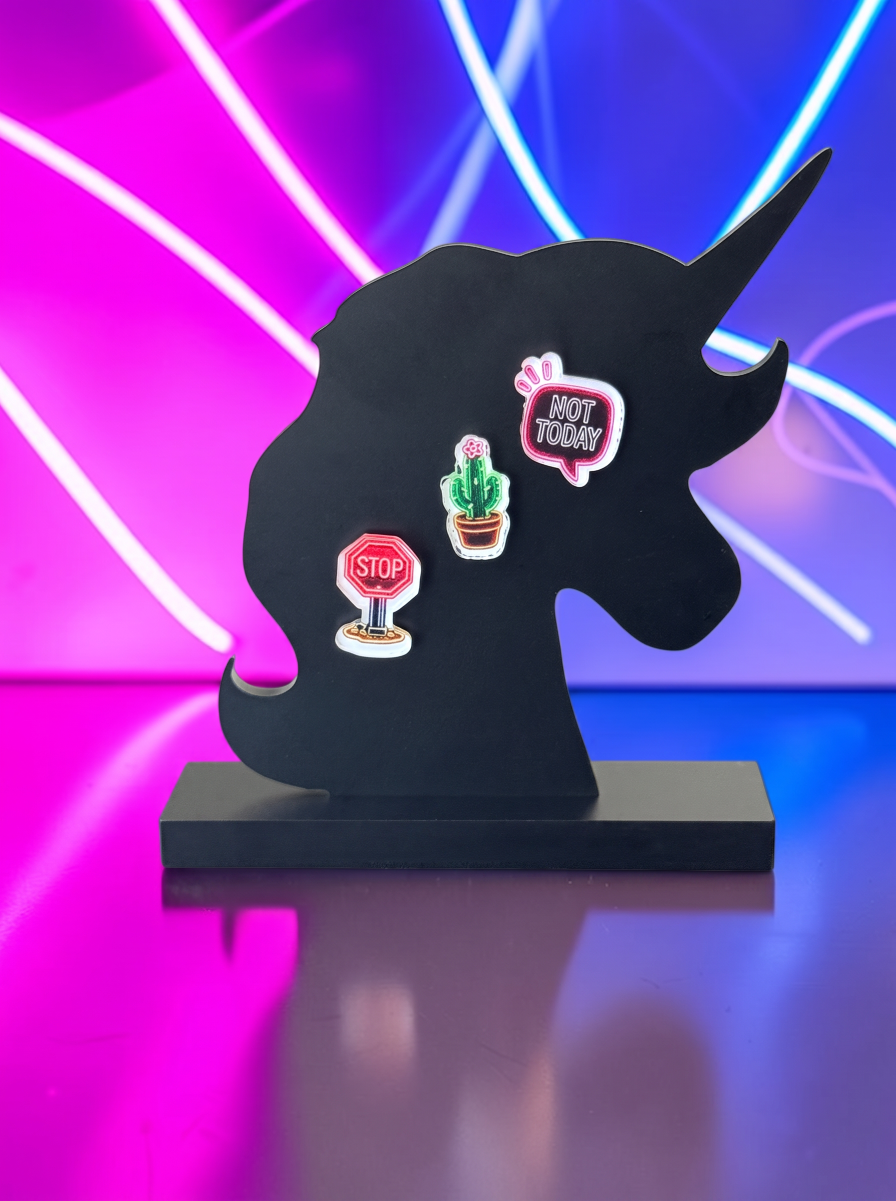 A black unicorn-shaped acrylic stand with three whimsical earrings attached, set against a vibrant pink and blue neon light background.