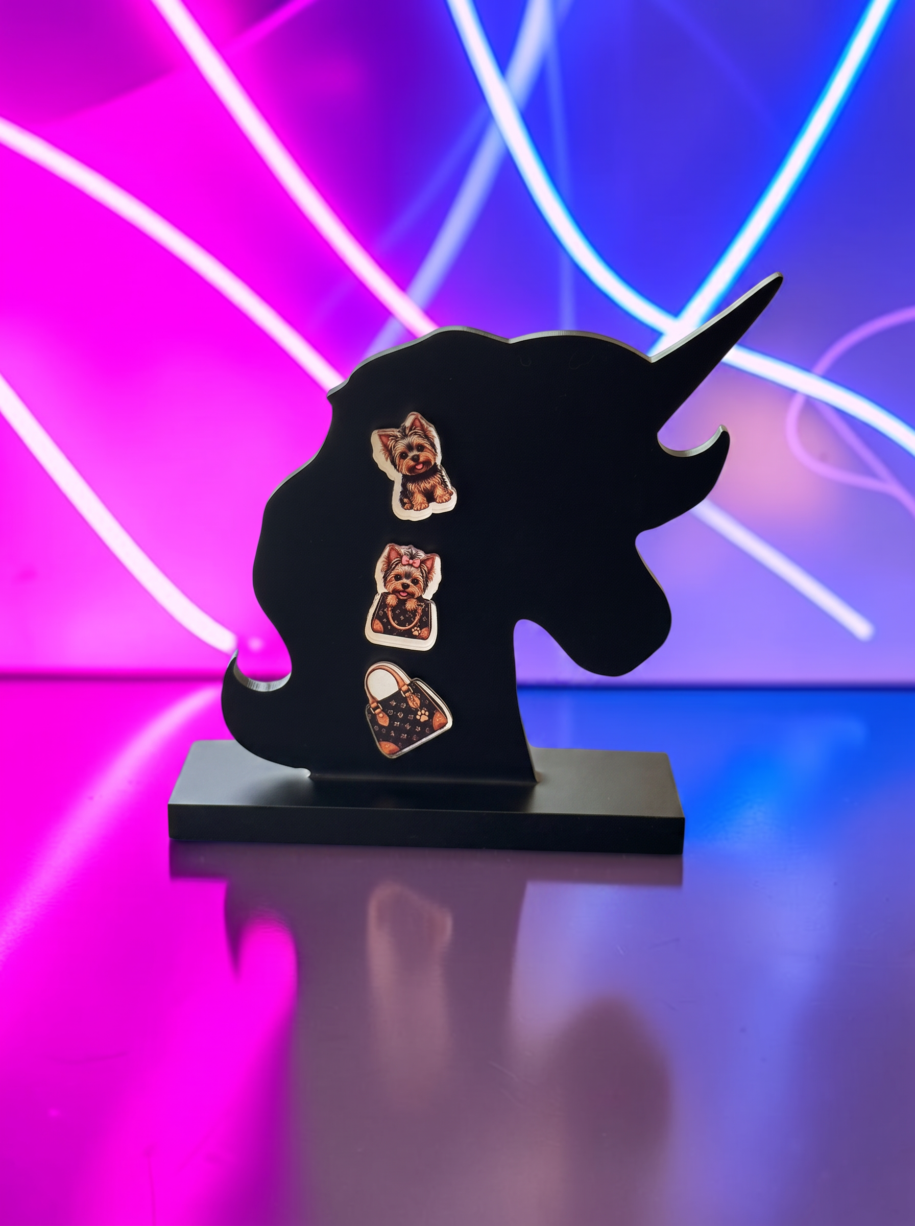 Three small rectangular jewelry pieces with a brown and orange patterned center and white borders, displayed on a black unicorn-shaped stand against a neon pink and blue background.
