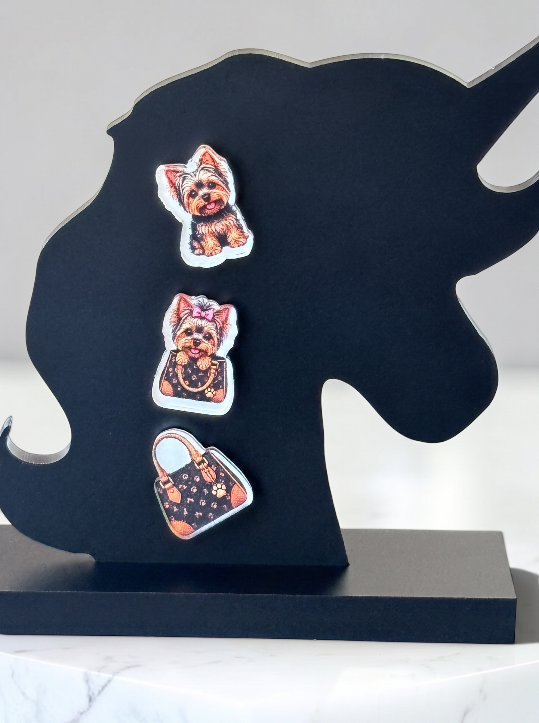 A black unicorn-shaped decorative stand on a matching base, featuring three small illustrated earrings shaped like a dog, a cat, and a handbag, displayed against a light neutral background.