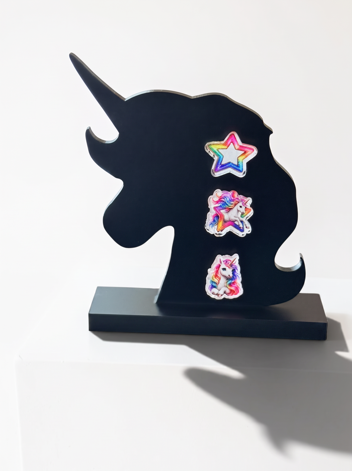 A black unicorn-shaped decorative plaque or stand on a rectangular base, decorated with three colorful earrings, photographed against a plain white background.