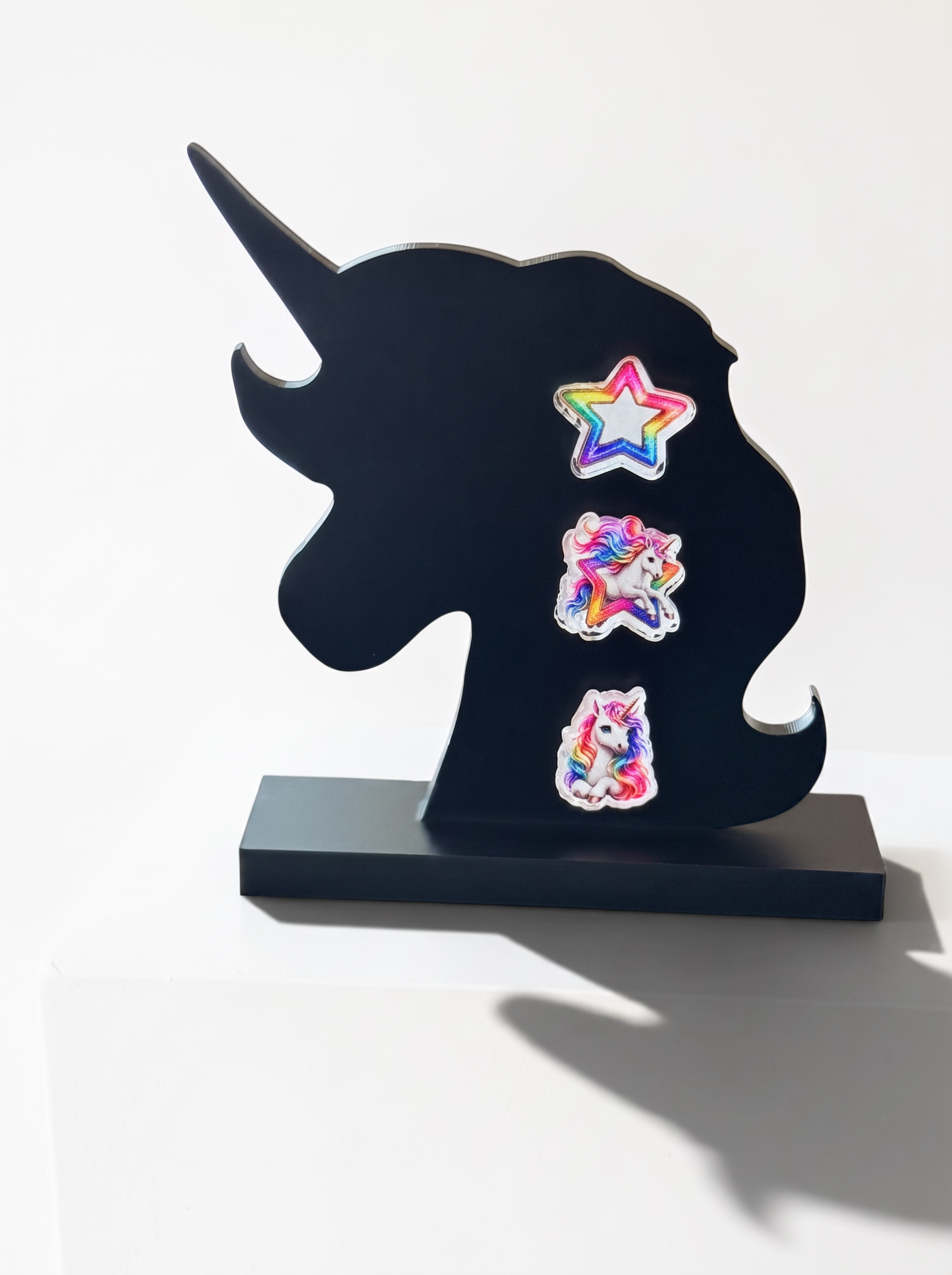 A black unicorn-shaped decorative plaque or stand on a rectangular base, decorated with three colorful earrings, photographed against a plain white background.