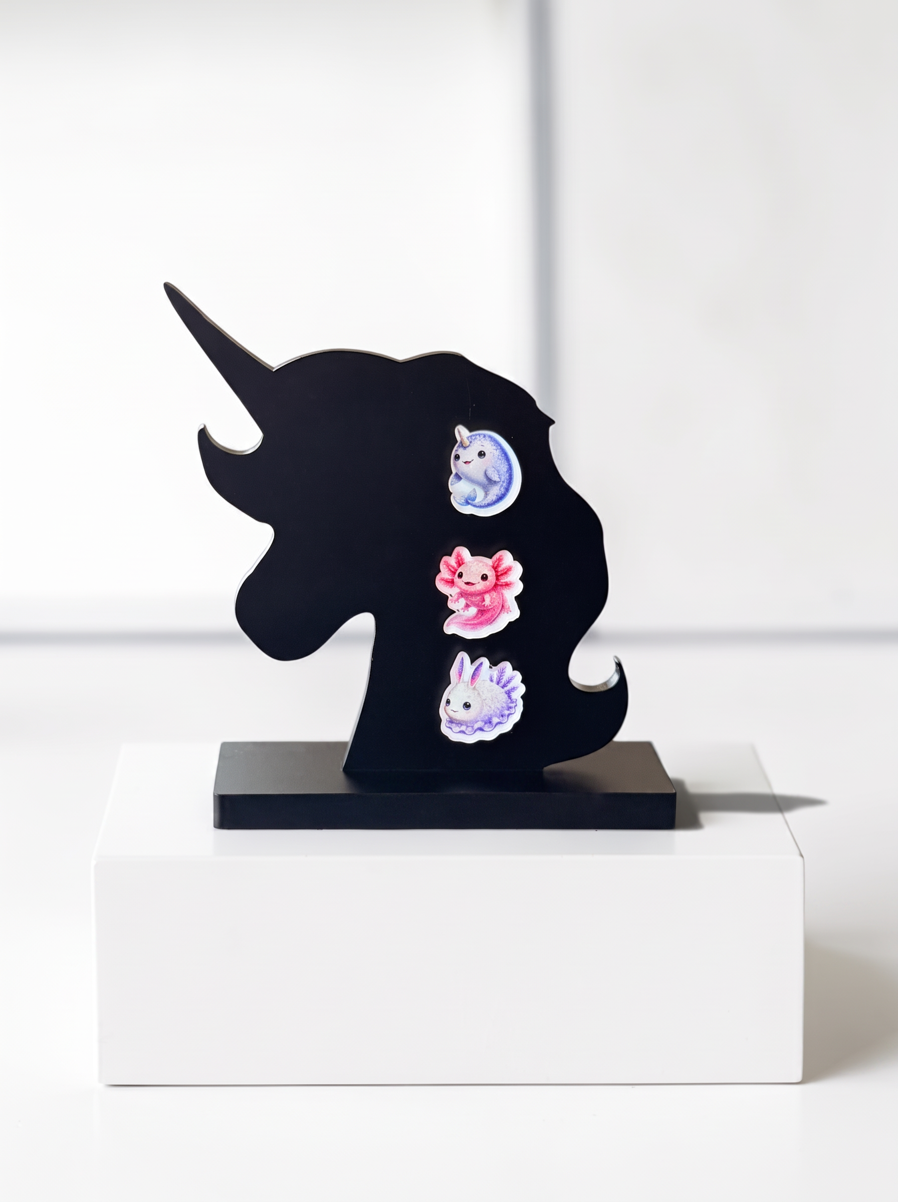 A black acryli  unicorn-shaped wall decor piece with three colorful earrings. The earrings include a blue Narwhal, a pink Axolotl and a Sea Bunny which are all cute and weird at the same time. 